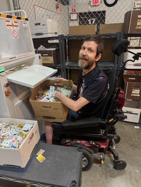 Man with beard sitting shredding paper in front of shredding machine