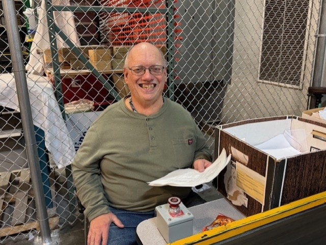 A man smiling in front of a conveyor belt shredder shredding confidential material