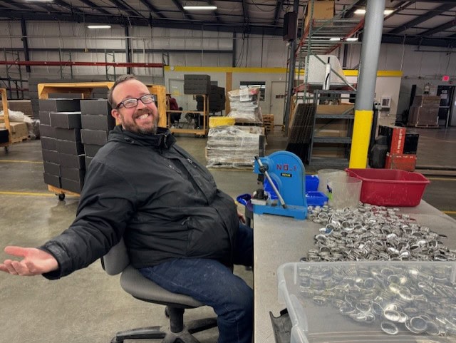 Button work with a big smile! Man with classes sitting in front of table working on buttons- hands are back with a big smiile