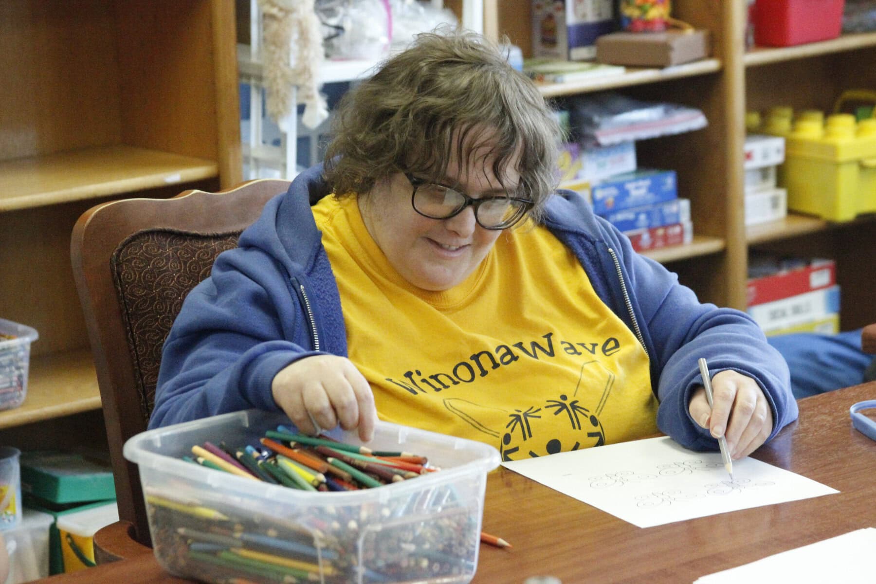 Creating in the SPARK classroom A woman smiling as she is coloring a paper in the SPARK classroom