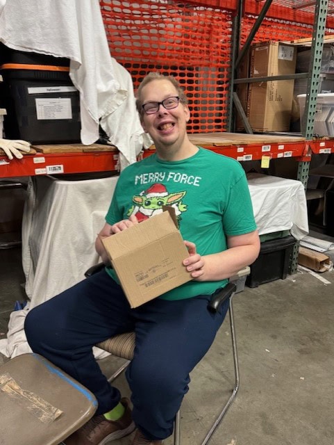 A man sitting smiling and taking apart cardboard boxes to crush