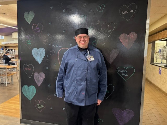 26 years of service at Chartwells on Winona State’s food service Man in food service uniform standing by sign at Winona State University